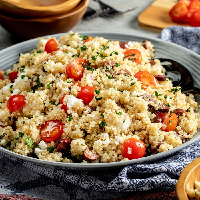 A bowl of quinoa salad with cherry tomatoes, olives, and feta cheese.
