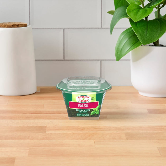 A single container of Gourmet Garden Basil (Case Of 72) sits on a light wood countertop, with a white tiled backsplash and a green plant in the background.