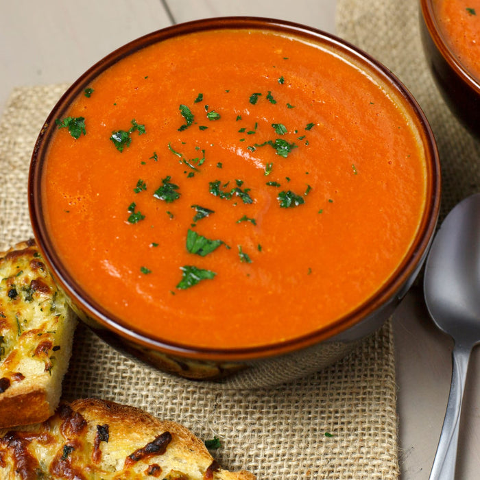 A bowl of tomato soup with parsley garnish and two slices of toasted bread.