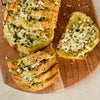 A delicious loaf of cheesy garlic bread, generously seasoned with Gourmet Garden Lightly Dried Italian Seasoning Blend 0.52 Oz, is sliced and served on a rustic wooden board.