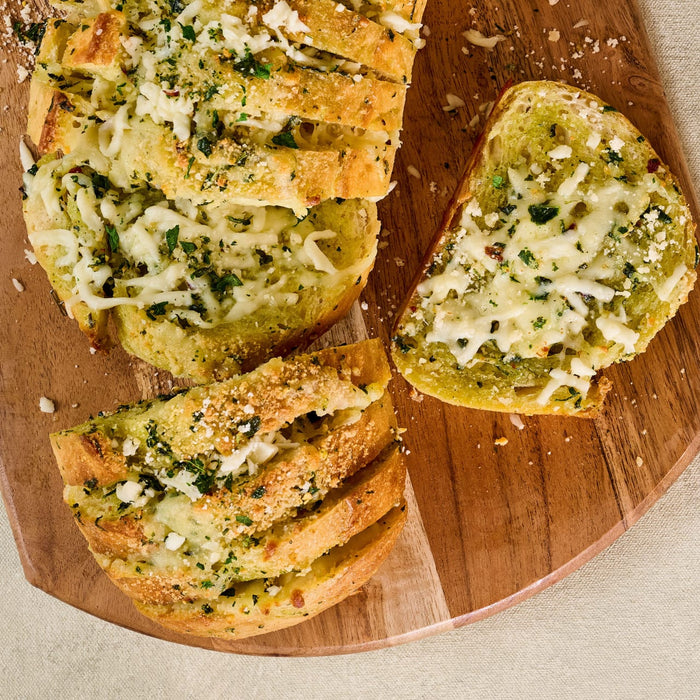 A delicious loaf of cheesy garlic bread, generously seasoned with Gourmet Garden Lightly Dried Italian Seasoning Blend 0.52 Oz, is sliced and served on a rustic wooden board.