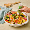 A person is adding Gourmet Garden basil paste to a bowl of colorful sauteed vegetables.