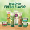 A variety of Gourmet Garden products, including ginger, garlic, basil, and onion, are displayed against a blurred green background to highlight their fresh flavor.