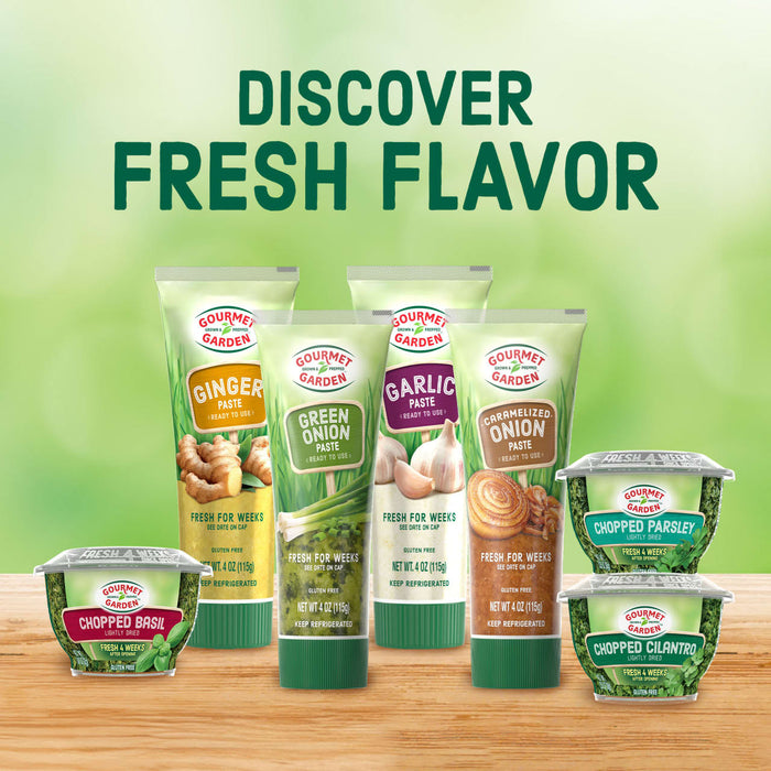 A variety of Gourmet Garden products, including ginger, garlic, basil, and onion, are displayed against a blurred green background to highlight their fresh flavor.