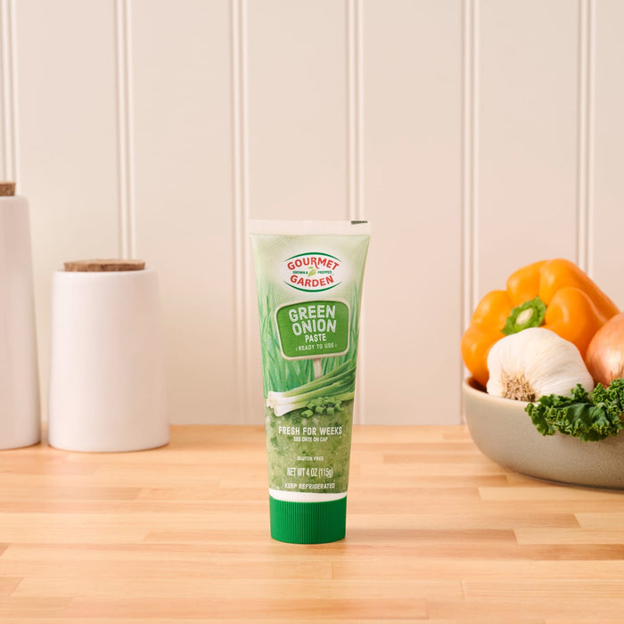 A tube of Gourmet Garden Green Onion Stir-In Paste sits on a wooden countertop in a kitchen setting.