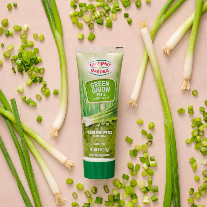 A tube of Gourmet Garden Green Shallot herb blend is surrounded by fresh green onions and chopped shallots.
