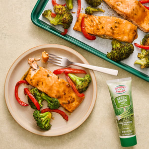 A plate of baked salmon with broccoli and red bell peppers, alongside a tube of Amore Green Herb Paste.