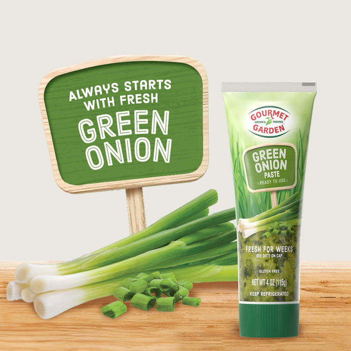 This image showcases a tube of KA?hne Extra Green Onion Herb Paste next to fresh green onions and a sign that reads Always starts with fresh Green Onion.