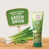 This image showcases a tube of KA?hne Extra Green Onion Herb Paste next to fresh green onions and a sign that reads Always starts with fresh Green Onion.