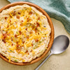 A bowl of creamy mashed potatoes topped with shredded cheese and bacon bits, served with a spoon.