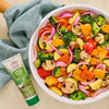 A colorful bowl of roasted vegetables, including broccoli, zucchini, mushrooms, red onion, and bell peppers, is displayed next to a tube of Amore Green Herb Paste.