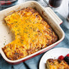A casserole dish filled with a cheesy breakfast casserole with a slice missing.