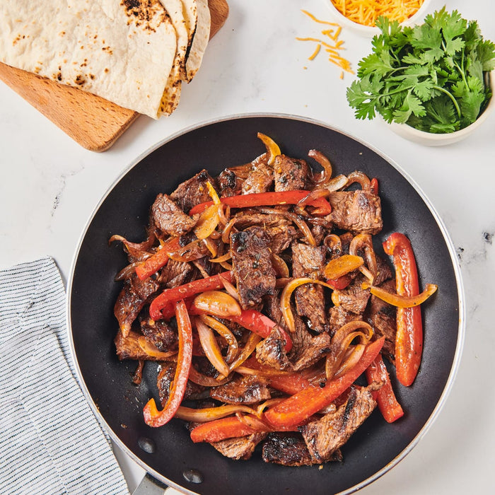 A close-up of a skillet filled with sliced steak red peppers and onions.