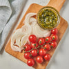 A wooden cutting board with sliced onions cherry tomatoes and a small bowl of green sauce.
