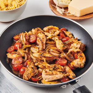 A close-up of a skillet with chicken tomatoes and onions.