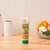 A tube of Amore brand onion paste stands on a wooden countertop next to fresh vegetables.