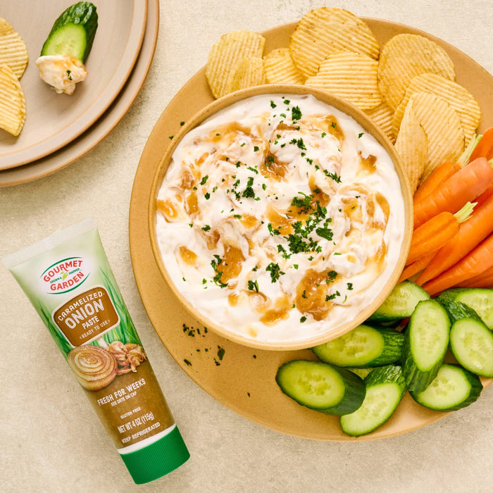 A bowl of Heluva Good! French Onion Dip with chips, carrots, and cucumbers, alongside a tube of the dip.