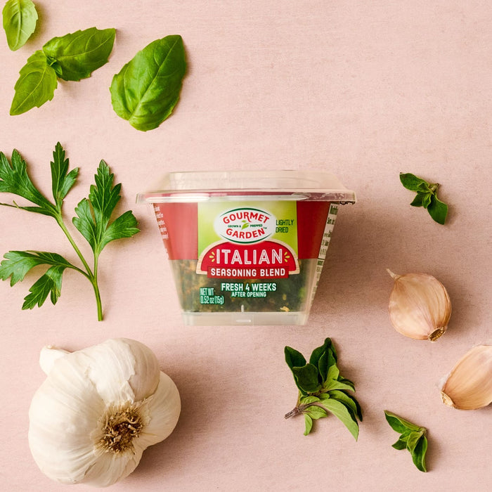 A container of Gourmet Garden Italian Seasoning Blend is surrounded by fresh basil, parsley, and garlic.