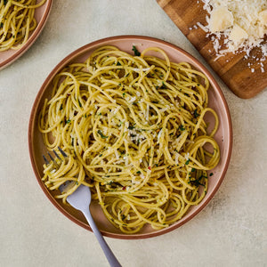 Overhead shot of a plate of spaghetti aglio e olio with grated cheese and a fork, alongside a wooden board with more cheese.