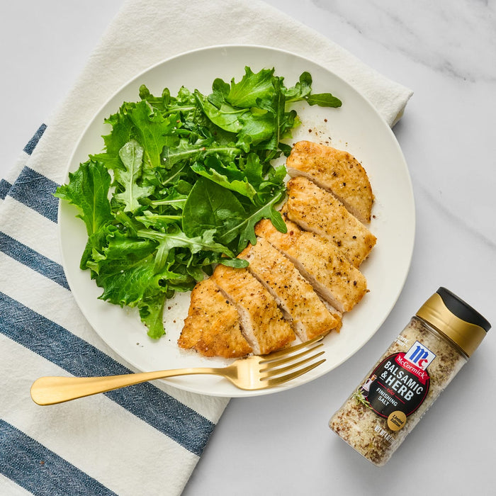 A plate of sliced chicken breast with a side of arugula and a shaker of McCormick Balsamic &amp; Herb Finishing Salt.