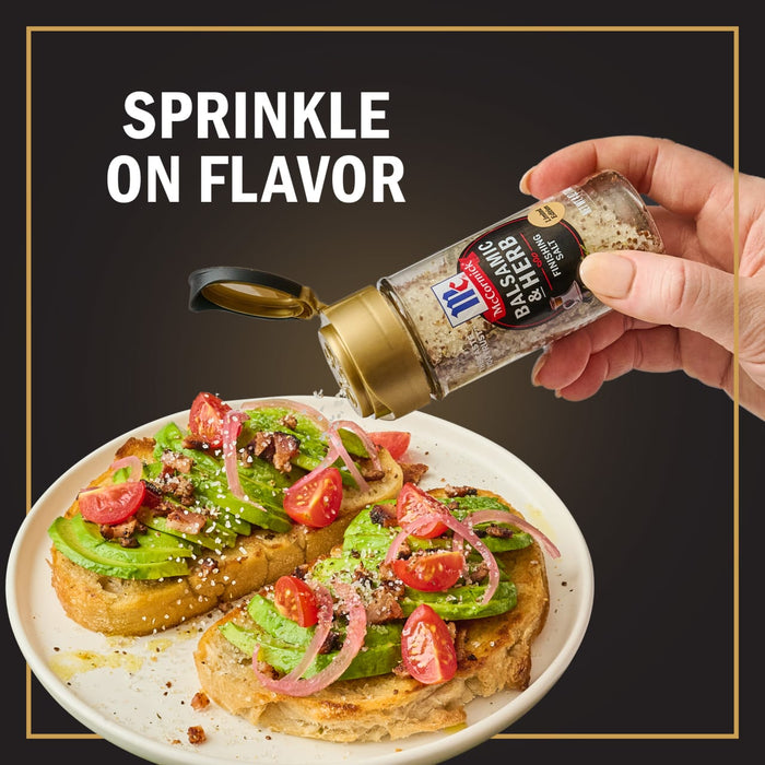 A hand sprinkles McCormick Balsamic &amp; Herb Finishing Salt onto avocado toast with tomatoes and red onions.