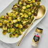 A white plate with roasted brussels sprouts and a gold spoon next to a bottle of McCormick Zesty Lemon Finishing Salt.
