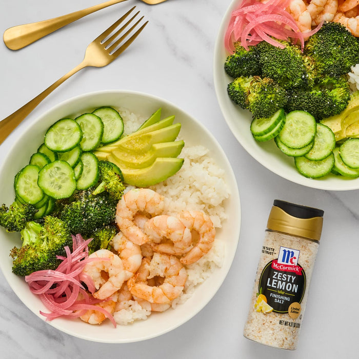 A bowl of shrimp rice avocado cucumber broccoli and red onion with a bottle of McCormick Zesty Lemon Finishing Salt.