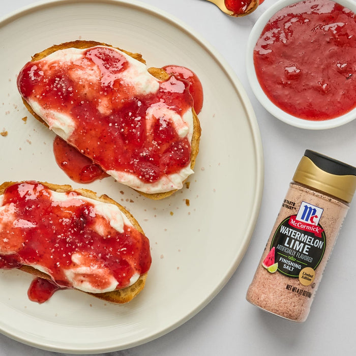 Two slices of bread topped with cream cheese and strawberry jam a small bowl of strawberry jam and a bottle of McCormick Watermelon Lime Finishing Salt.