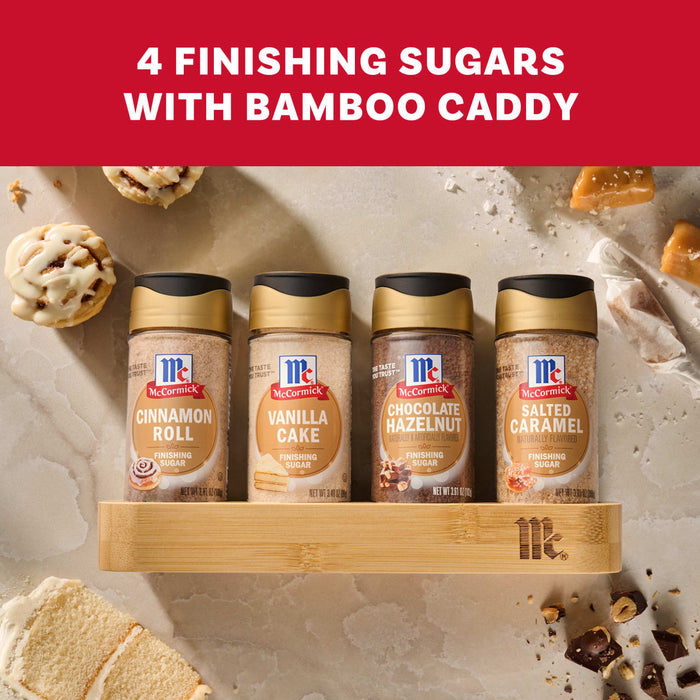 A package of the Mccormick Finishing Sugar Caddy 4Ct shows four bottles of finishing sugar in Cinnamon Roll, Vanilla Cake, Chocolate Hazelnut, and Salted Caramel flavors, all arranged in a bamboo caddy and surrounded by their corresponding sweet treats.
