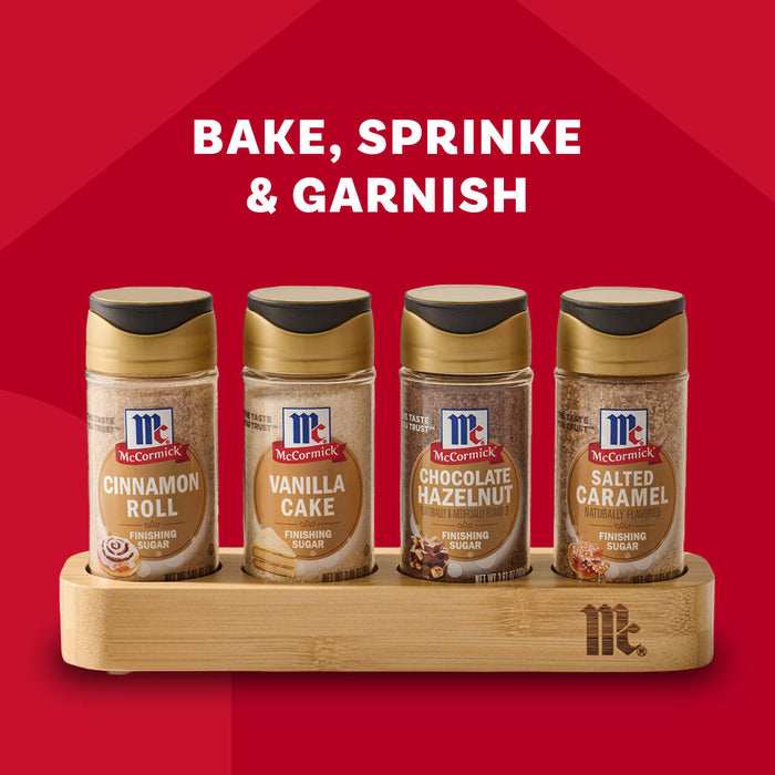 A Mccormick Finishing Sugar Caddy 4Ct is displayed against a red background, featuring four bottles of finishing sugar: Cinnamon Roll, Vanilla Cake, Chocolate Hazelnut, and Salted Caramel.