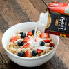 A bowl of oatmeal with blueberries and strawberries is being topped with Thai Kitchen coconut milk.