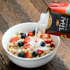 A bowl of oatmeal with blueberries and strawberries is being topped with Thai Kitchen coconut milk.