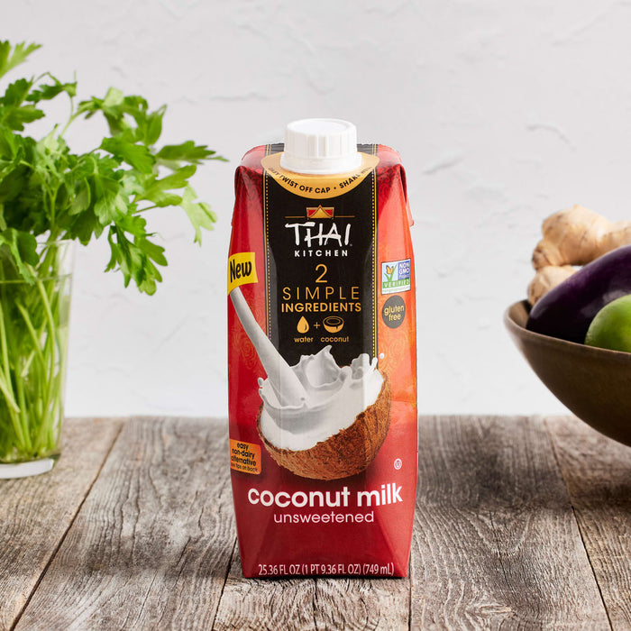 A carton of Thai Kitchen unsweetened coconut milk is displayed on a wooden surface with fresh ingredients.