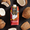 A carton of Thai Kitchen Simple coconut milk is surrounded by whole and halved coconuts.