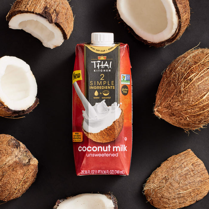 A carton of Thai Kitchen Simple coconut milk is surrounded by whole and halved coconuts.