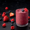 A vibrant berry smoothie is displayed in a glass with scattered fresh strawberries, raspberries, and blueberries around it.