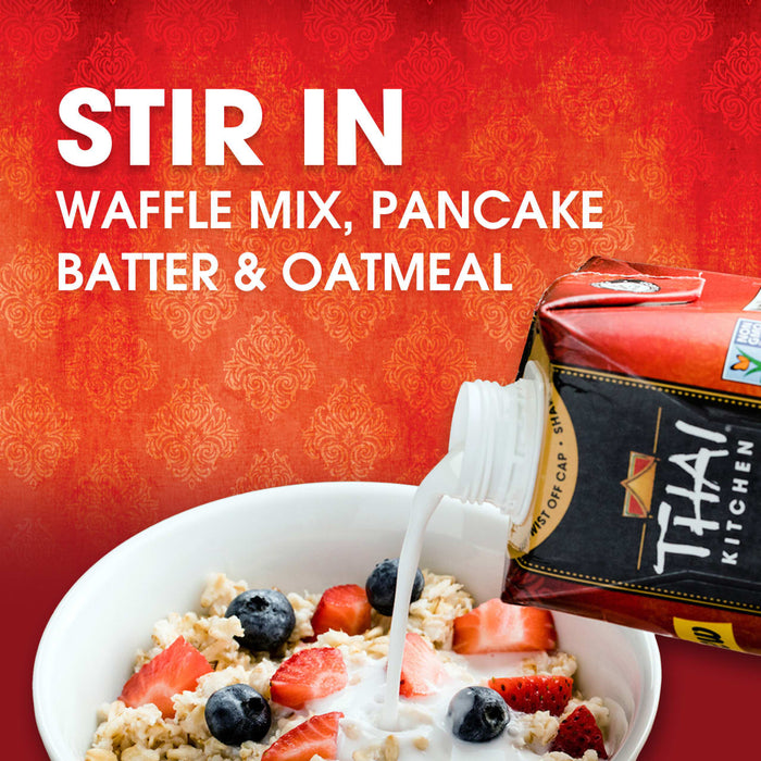 Thai Kitchen coconut milk is being poured into a bowl of oatmeal with strawberries and blueberries, suggesting it can be stirred into waffle mix, pancake batter, and oatmeal.