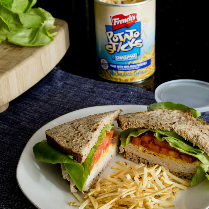 A turkey sandwich with lettuce and tomato on a plate with Frenchs Potato Sticks.