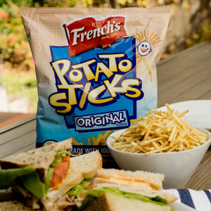 A bag of Frenchs Potato Sticks Original Flavor a bowl of potato sticks and two sandwiches.
