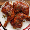 Three pieces of grilled chicken glazed with Sweet Baby Ray's barbecue sauce are arranged on a plate and garnished with herbs.