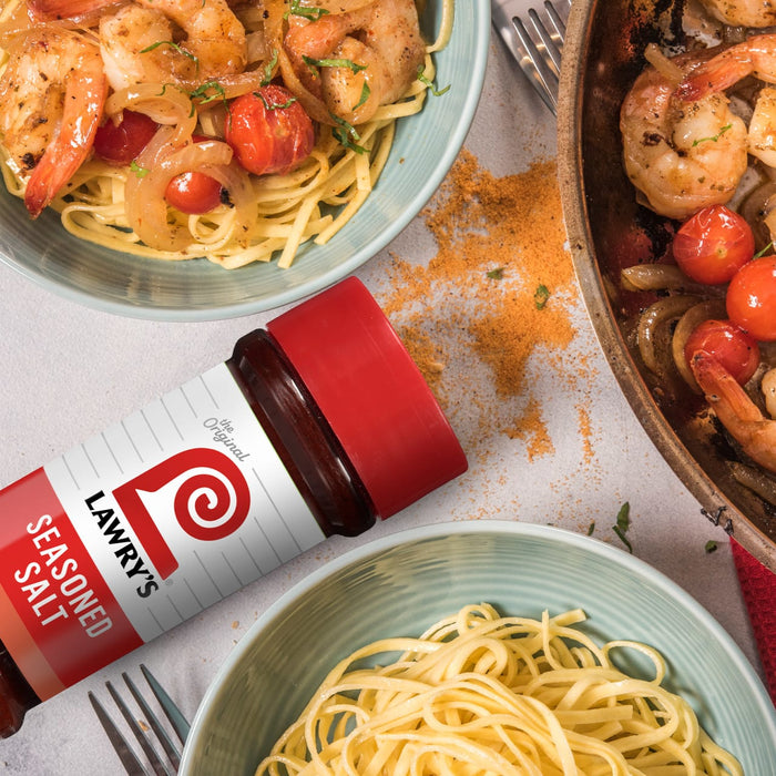 A bottle of Lawry's Seasoned Salt is featured next to plates of shrimp pasta, suggesting its use as a seasoning for the dish.
