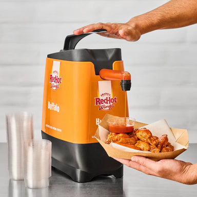 Orange and black Frank's RedHot Wings hot sauce dispenser with a bowl of wings and sauce.