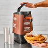A hand pours Cattlemens Memphis Sweet BBQ sauce onto a plate of french fries and chicken tenders.