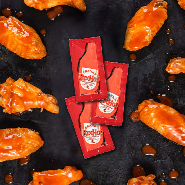 Three packets of Frank's RedHot Original Cayenne Pepper Sauce next to chicken wings.