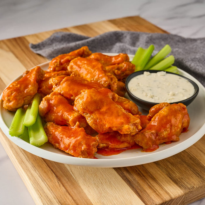 A plate of buffalo wings with celery sticks and blue cheese dip.