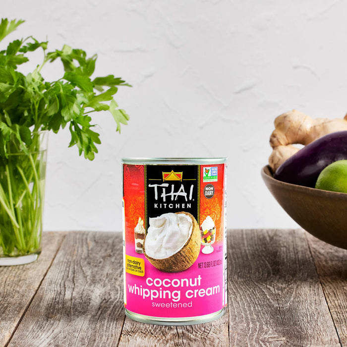 A can of Thai Kitchen coconut whipping cream sits on a wooden table next to a vase of parsley and a bowl of ginger eggplant and lime.