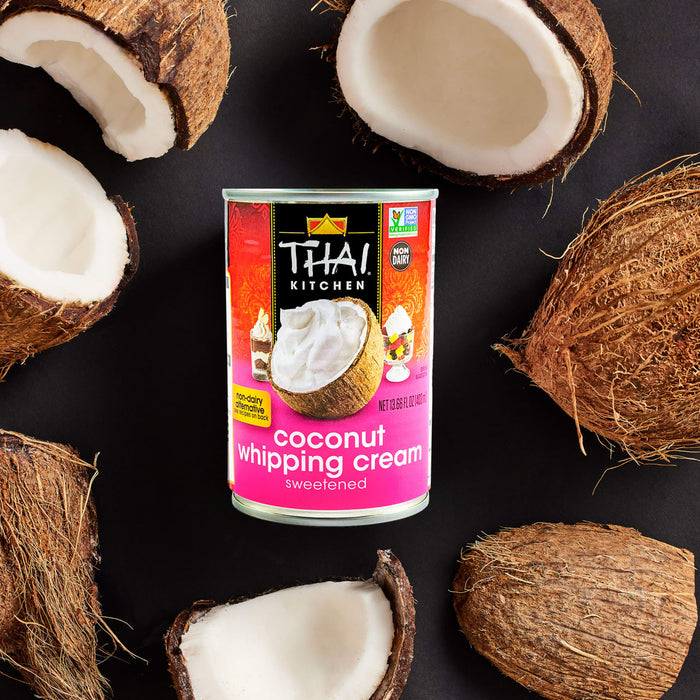 A can of Thai Kitchen coconut whipping cream is surrounded by halved coconuts.