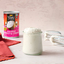 A can of Thai Kitchen coconut whipping cream sits next to a jar of whipped cream and beaters.