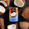 A can of Thai Kitchen evaporated coconut milk is surrounded by halved coconuts.