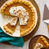 A delicious pumpkin pie topped with whipped cream and pecans sits on a table with a slice already served on a plate.